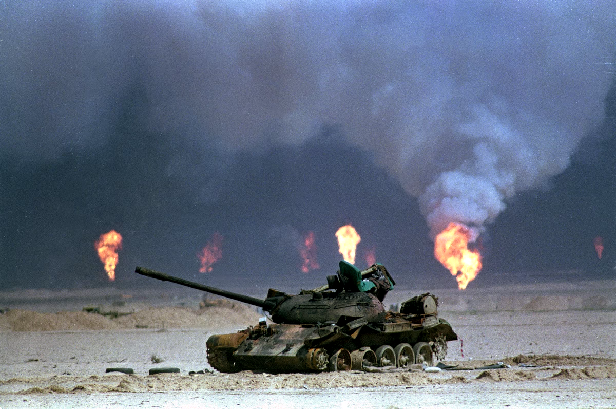 A destroyed tank set against distant fires.