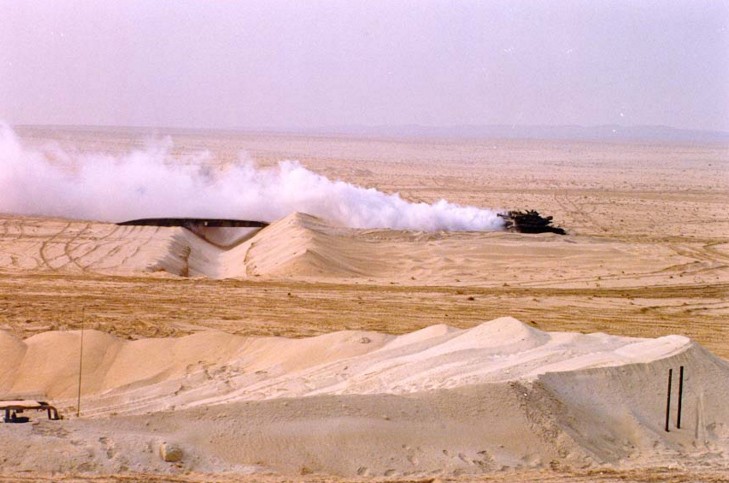 A smoking tank in a flat yellow desert.